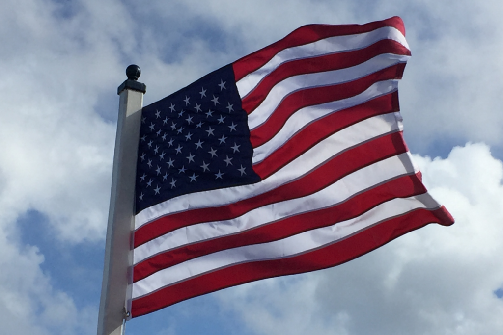 A flying US flag with sky behind it.